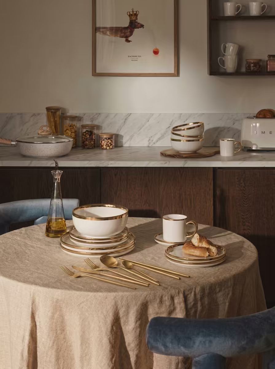 Warm dining table setting with dinnerware, mugs, cutlery and cookware